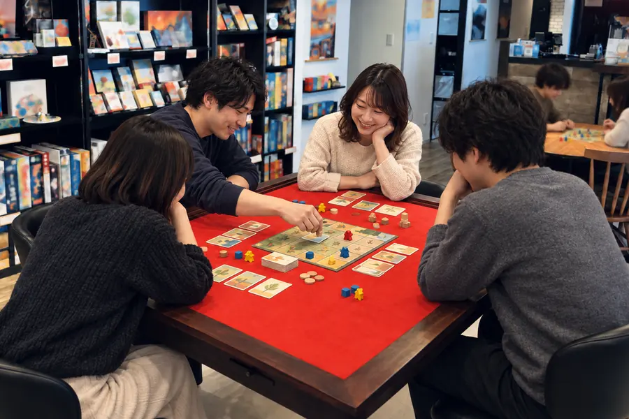 赤いゲーム卓を囲んで4人がボードゲームを遊んでいる様子